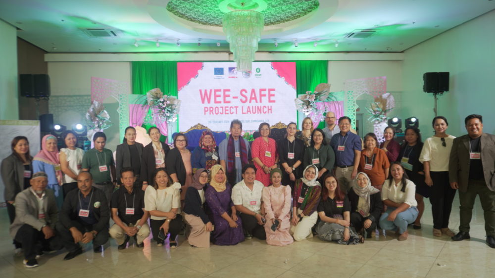 A group of people in a conference hall with the words WEE-SAFE Project Launch projected on the stage background